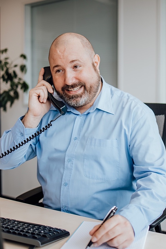 Mann in blauem Hemd am Schreibtisch sitzend und telefonierend