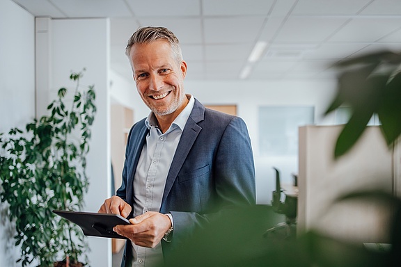 Mann in blauem Jackett mit Tablet in der Hand und lächelnd 