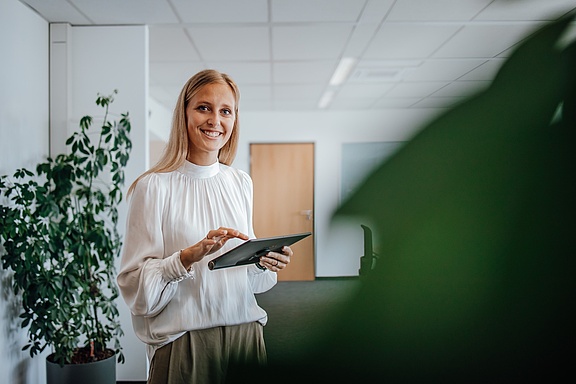 Blonde Frau mit Tablet in der Hand in die Kamera lächelnd