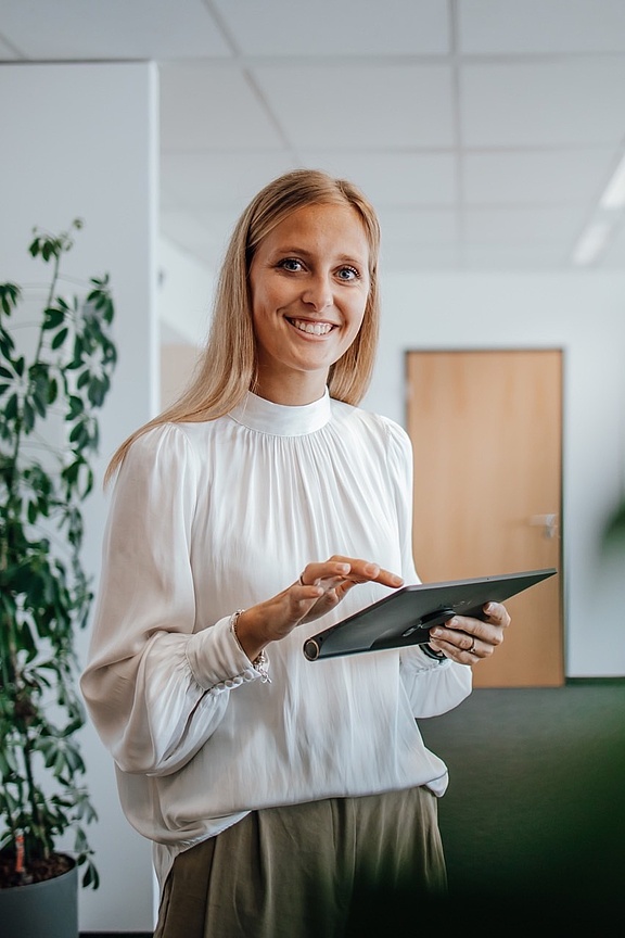 Blonde Frau mit Tablet in der Hand in die Kamera lächelnd