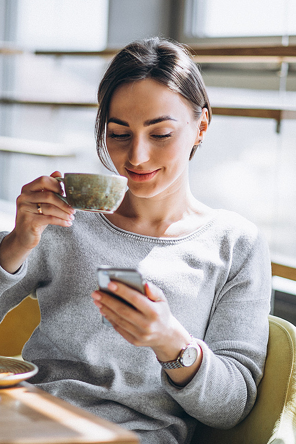 Frau am Tisch sitzend mit Kaffeetasse in der Hand und Laptop vor sich