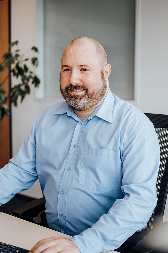 Mann in blauem Hemd am Schreibtisch sitzend mit Headset