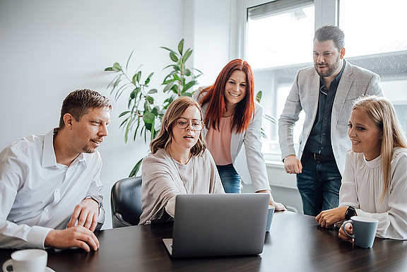 Team um einen Tisch mit Laptop herum im Gespräch